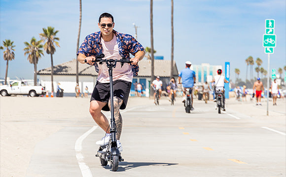 man crouching while riding electric scooter down beach boardwalk