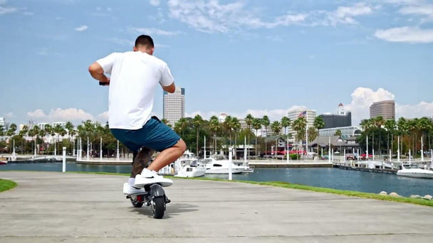 Back of man crouching while riding scooter on beach boardwalk on sunny day