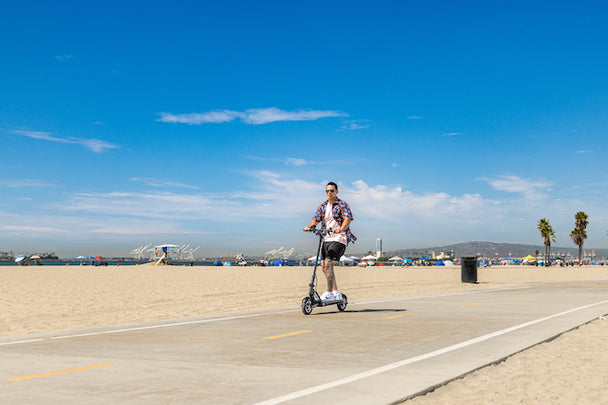 Man riding scooter on beach boardwalk wearing sunglasses on a beautiful day